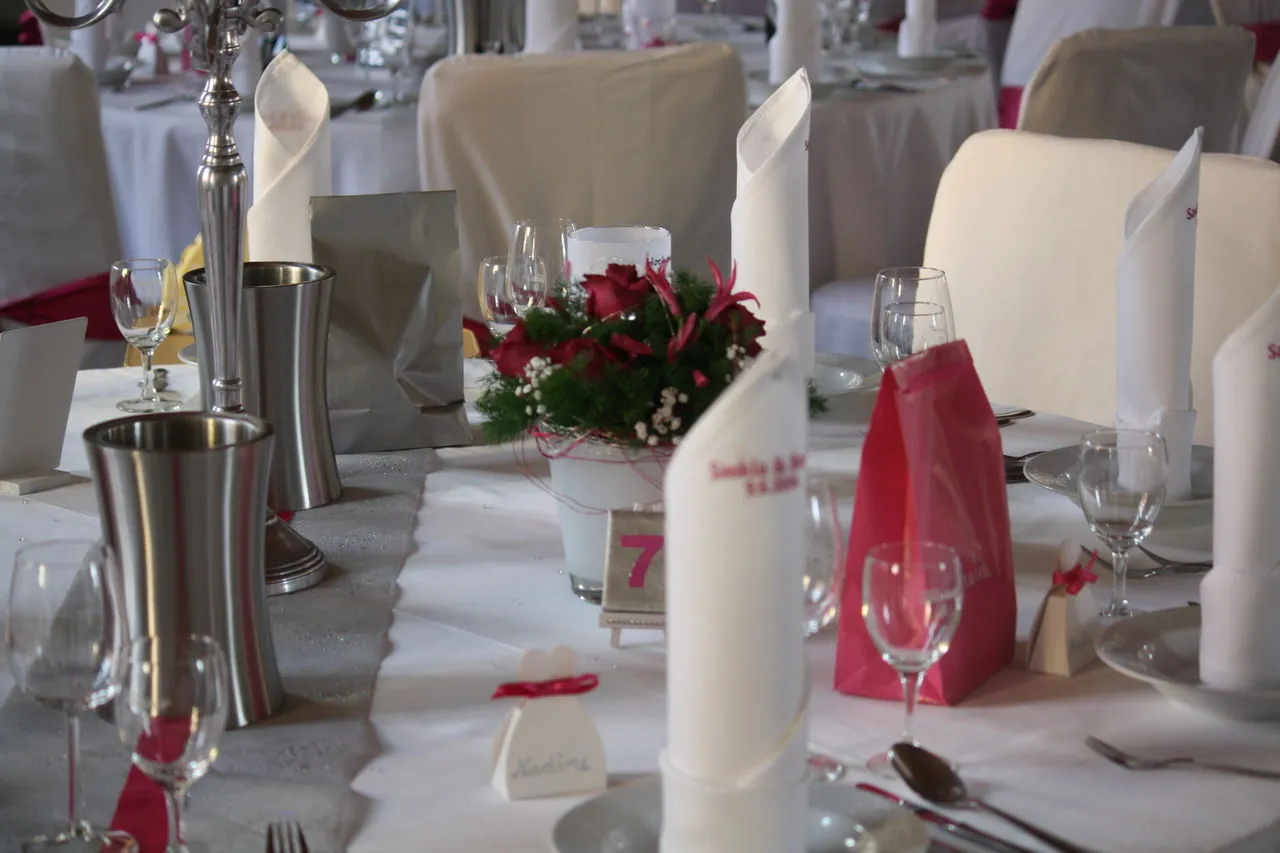 Hochzeitstafel mit rotem Blumengesteck, Kerzen und Tischkarten